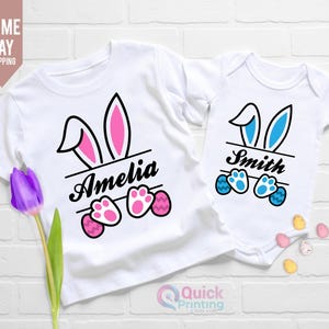 May include: Two white t-shirts with bunny ears and paw prints. The larger shirt says "Amelia" and the smaller shirt says "Smith".