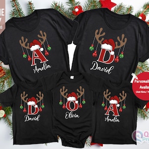 May include: Black Christmas family t-shirts with reindeer antlers, Santa hats, and personalized initials and names. The shirts feature red and green ornaments. The text "Personalisation Available" is visible.
