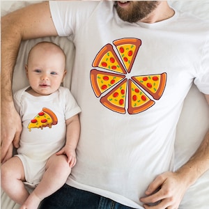 May include: A white t-shirt featuring a pizza graphic. The pizza is divided into six slices, each with red pepperoni, green peppers, and yellow cheese. A white babygrow with a single slice of pizza is shown on a baby.