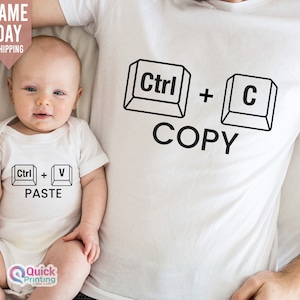Può includere: Due magliette bianche con una grafica in bianco e nero di tasti del computer. La maglietta per adulti dice "Ctrl + C COPIA" e la tutina per neonati dice "Ctrl + V INCOLLA".