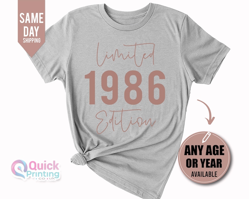 May include: A light gray short-sleeve t-shirt featuring the text Limited 1986 Edition in a muted rose color. The word Limited and Edition are written in a cursive script font, while the number 1986 is displayed in a large, bold, sans-serif font.