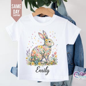 May include: White t-shirt with a watercolour illustration of a floral bunny. The design includes colourful tulips, lavender, and heart-shaped accents. The name "Emily" is printed in a script font below the bunny.