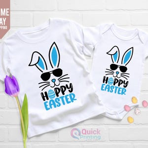 May include: Two white t-shirts featuring a blue bunny wearing sunglasses and the text "Hoppy Easter". The larger shirt has an Easter egg graphic.