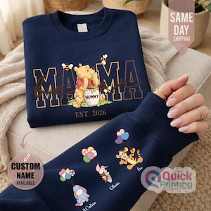 Puede incluir: Sudadera azul marino con dise&ntilde;o de Winnie the Pooh, la palabra "MAMA" y "EST. 2026". La manga muestra personajes de dibujos animados con globos y nombres. Una sudadera c&oacute;moda e informal.