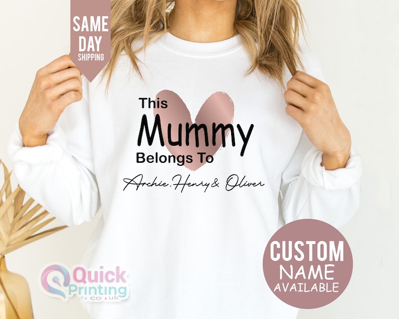 May include: White sweatshirt with the text "This Mummy Belongs To Archie, Henry & Oliver" and a pink heart design. The sweatshirt also has text that says "Custom Name Available" and "Same Day Shipping".