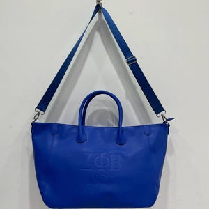 May include: A bright blue leather tote bag with a shoulder strap. The bag has a large embossed logo that says "ZOB 1920".