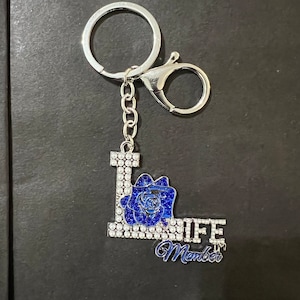 May include: A silver keychain with a blue and white rhinestone letter L, a blue rhinestone rose, and the words "Life Member".