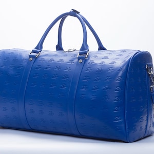 May include: A bright blue leather duffel bag with a repeating embossed pattern. The bag has two top handles and a detachable shoulder strap.