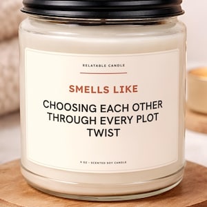 May include: A clear glass jar candle with a black metal lid, filled with white wax. The label reads RELATABLE CANDLE, SMELLS LIKE CHOOSING EACH OTHER THROUGH EVERY PLOT TWIST, and 9 OZ SCENTED SOY CANDLE in black and brown text on a cream background.