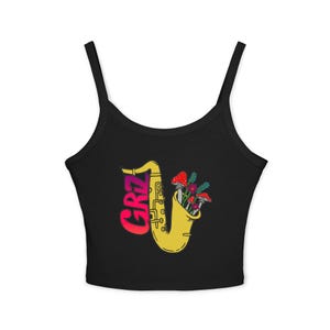 May include: Black crop top with a colorful graphic. The design features a yellow saxophone with red and pink text that reads "GRIZ". The saxophone's bell is filled with colorful mushrooms and flowers. The top has thin straps.