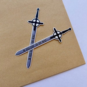 May include: Two silver sword stickers with black details and the text "In this life or the next" on them. The stickers are crossed over each other.