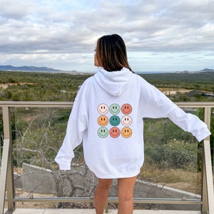 May include: White hoodie with a back design of nine colorful smiley faces arranged in a 3x3 grid.