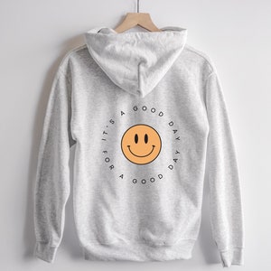 May include: A gray hooded sweatshirt with a yellow smiley face and the text "A GOOD DAY FOR A GOOD DAY" in a circle on the back.