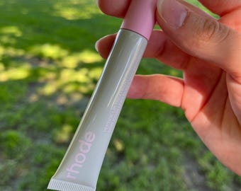 May include: A white tube of lip treatment with a pink cap and a silver key ring attached. The tube is labeled "rhode" and "peptide lip treatment, smooth out lines & plump lips".