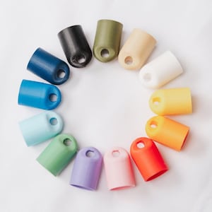 May include: A set of 14 colorful plastic caps with a hole in the center. The caps are arranged in a circle, with the colors ranging from dark green to light pink.