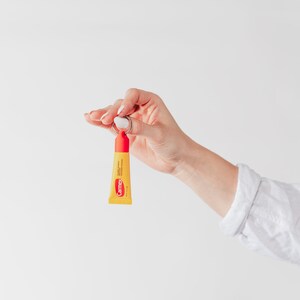 K&ouml;nnte beinhalten: Eine Hand h&auml;lt eine kleine gelbe Tube Carmex Lippenbalsam, die an einem silbernen Schl&uuml;sselring befestigt ist. Der Lippenbalsam ist mit "Carmex" und "Lippenbalsam mit Sonnenschutz SPF 15" beschriftet.