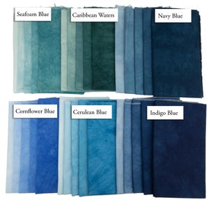 K&ouml;nnte beinhalten: Eine Sammlung von Stoffmustern in zwei Reihen, die verschiedene Blau- und T&uuml;rkist&ouml;ne zeigen. Die Beschriftungen umfassen Seafoam Blue, Caribbean Waters, Navy Blue, Cornflower Blue, Cerulean Blue und Indigo Blue. Jedes St&uuml;ck weist eine gesprenkelte, texturierte Optik mit unterschiedlicher Farbintensit&auml;t auf.