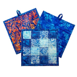May include: Three blue and white quilted pot holders with different patterns. The pot holders have a loop for hanging.