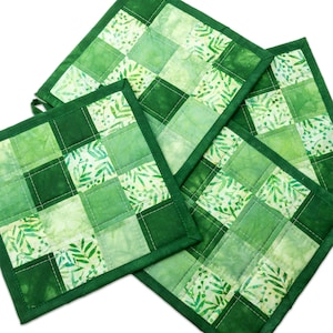 May include: Four square quilted pot holders in shades of green. Each pot holder features a patchwork design with varying shades of green squares and leaf patterns. The edges are finished with a dark green binding.