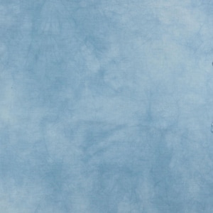 K&ouml;nnte beinhalten: Ein hellblauer Stoff mit einem subtilen, gesprenkelten Batikmuster. Die Oberfl&auml;che weist weiche, wolkenartige Variationen in der Farbintensit&auml;t auf, die von blassem Himmelblau bis zu etwas tieferen T&ouml;nen reichen und eine texturierte Optik erzeugen.