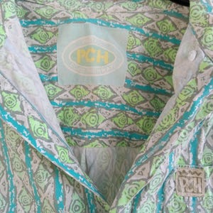 May include: A button-down shirt with a geometric pattern in shades of gray, teal, and lime green. The shirt features a collar and a chest pocket with the letters "PCH". The shirt has a label that says "PCH Coast Highway".