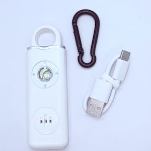 May include: A white personal safety alarm with a built-in LED light and a black carabiner clip. Includes a USB charging cable. The alarm has a loop for attaching to a keychain or bag. The device is designed for personal safety.