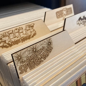 Può includere: Divisori in legno per fumetti con loghi di supereroi incisi al laser. I loghi includono "Hulk", "The Amazing Spider-Man", "She-Hulk" e "Batman".