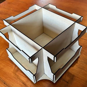 May include: A wooden organizer with multiple compartments, perfect for storing small items. The organizer is made of light wood with black edges and has a two-tier design.