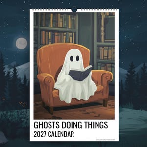 May include: A 2027 wall calendar titled Ghosts Doing Things, featuring an illustration of a white ghost sitting in a brown armchair reading a book in a library. The calendar has a spiral binding at the top and a white border around the central image.