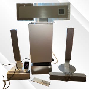 May include: A silver home theater system with a DVD player, subwoofer, speakers, and remote control. The system includes a main unit with a DVD label, two tall speakers, a sound bar, and a remote.