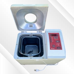 May include: An open, off-white Regal bread maker with a red control panel. The bread maker has a rectangular baking pan and a hinged lid. The control panel features buttons for menu selection, delay timer, and color.