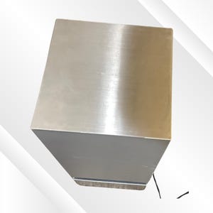 May include: A stainless steel, rectangular box with a brushed metal finish. The box has a solid, geometric design, with a slightly angled top and a smooth, reflective surface. The object is likely a container or storage unit.