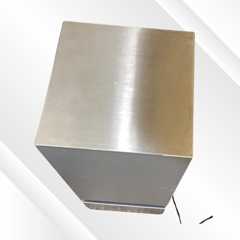 May include: A stainless steel, rectangular box with a brushed metal finish. The box has a solid, geometric design, with a slightly angled top and a smooth, reflective surface. The object is likely a container or storage unit.