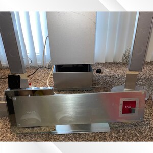 May include: A silver Sony DVD home theater system with a brushed metal finish. The system includes a main unit with a glass front, a subwoofer, and four speakers. The DVD player is visible on the front panel.