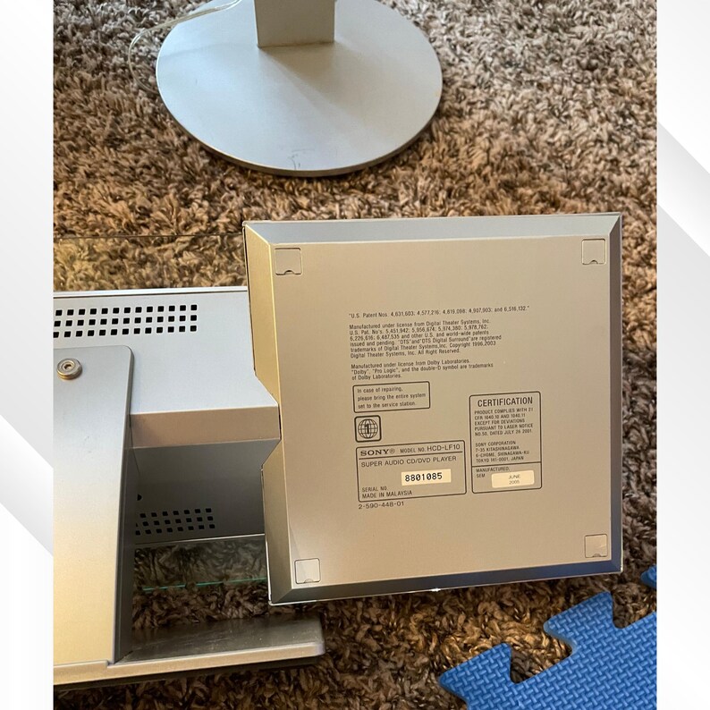 May include: Silver Sony HCD-LF10 Super Audio CD/DVD player. The device is rectangular with a series of small holes on the side. The back of the device has a certification label and the text "SUPER AUDIO CD/DVD PLAYER".
