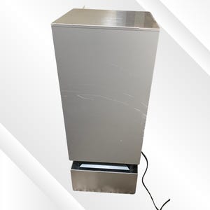 May include: A tall, silver-colored appliance with a rectangular shape. The top and bottom sections are metallic, while the main body has a matte finish. A black power cord extends from the bottom. Scratches are visible on the side.