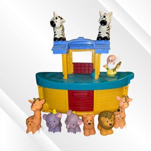May include: A plastic toy Noah's Ark playset featuring a yellow hull, a teal deck, and a blue roof. Included are two zebra figures on the roof, a bearded human figure, and six animal figures: two giraffes, two elephants, a bear, and a lion.