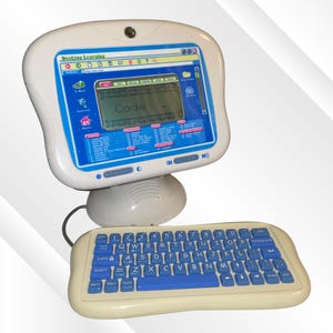 May include: A white and blue Desktop Learning toy computer with a small screen displaying the word "Code". The keyboard has blue keys and a cream-colored base. The computer has a mouse attached.