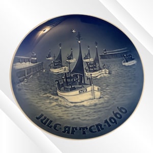 May include: A blue and white decorative plate featuring a nautical scene with several sailboats on the water. The plate has a dark blue border and the text "Jule Aften 1966" is inscribed at the bottom. A star is at the top.