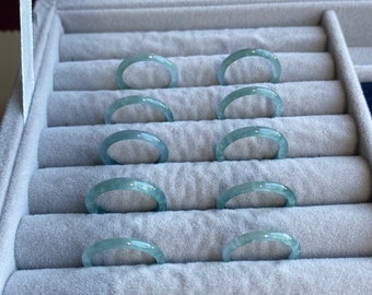 May include: A set of eight jadeite jade rings in a velvet-lined ring box. The rings are a pale green color and are arranged in rows.