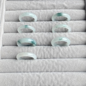 May include: Seven jade rings in a ring sizing display. The rings are a light green color with darker green veins.