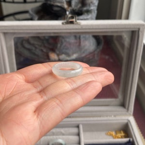 May include: A white jade ring with a smooth, polished surface. The ring is displayed on a hand, showcasing its size and shape.