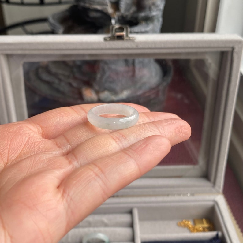 May include: A white jade ring with a smooth, polished surface. The ring is displayed on a hand, showcasing its size and shape.
