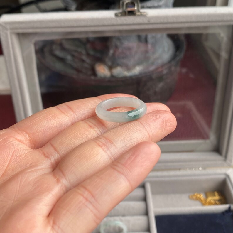 May include: A white jade ring with a green jade inlay. The ring is shown on a hand.