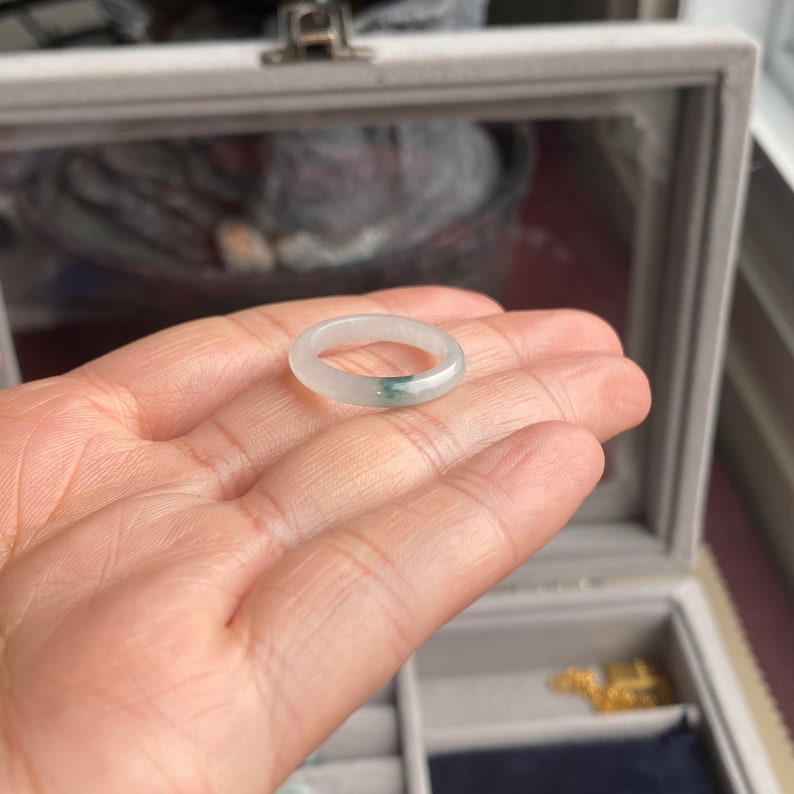 May include: A white jade ring with a green jade band. The ring is shown on a hand.