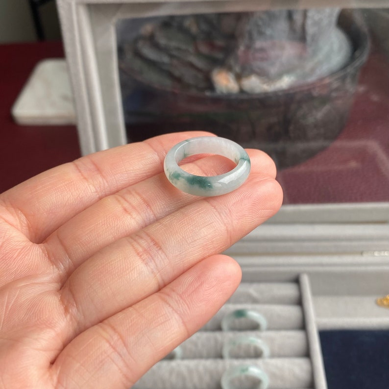 May include: A jade ring with a white base and green swirls. The ring is shown on a hand.