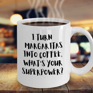 Könnte beinhalten: Eine weiße Kaffeetasse mit schwarzem Text, der lautet: "Ich verwandele Margaritas in Kaffee, was ist deine Superkraft?"