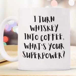 Könnte beinhalten: Eine weiße Kaffeetasse mit schwarzem Text, der lautet: "Ich verwandele Whisky in Kaffee, was ist deine Superkraft?"