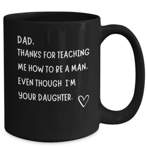 Könnte beinhalten: Schwarze Kaffeetasse mit weißem Text, der lautet: "DAD. THANKS FOR TEACHING ME HOW TO BE A MAN. EVEN THOUGH I'M YOUR DAUGHTER." mit einem kleinen Herzsymbol.
