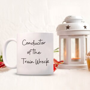 May include: White ceramic coffee mug with black text that reads "Conductor of the Train Wreck".